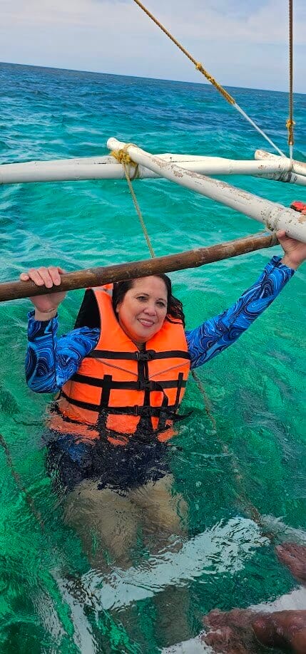 Woman in orange life vest enjoying clear turquoise waters in Boracay, Philippines, holding onto a boat ladder.