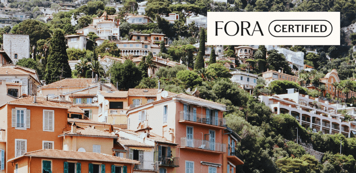 Hillside Mediterranean village with orange rooftops, lush greenery, and "FORA Certified" logo in the corner.